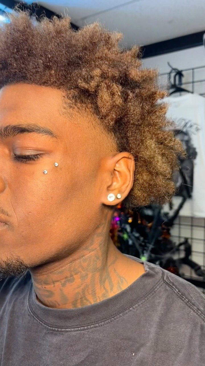 Man with curly hair showing two silver stud piercings above his right eyebrow.
