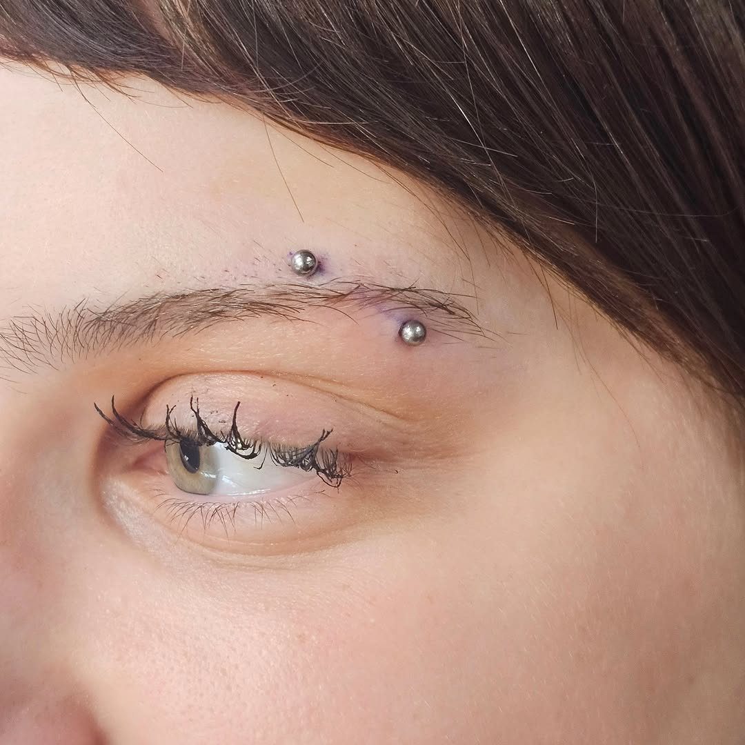 Two silver ball stud piercings placed horizontally along a person's eyebrow.