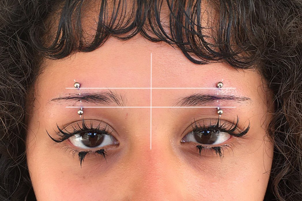 Person with matching silver barbell piercings on both eyebrows and graphic alignment lines.
