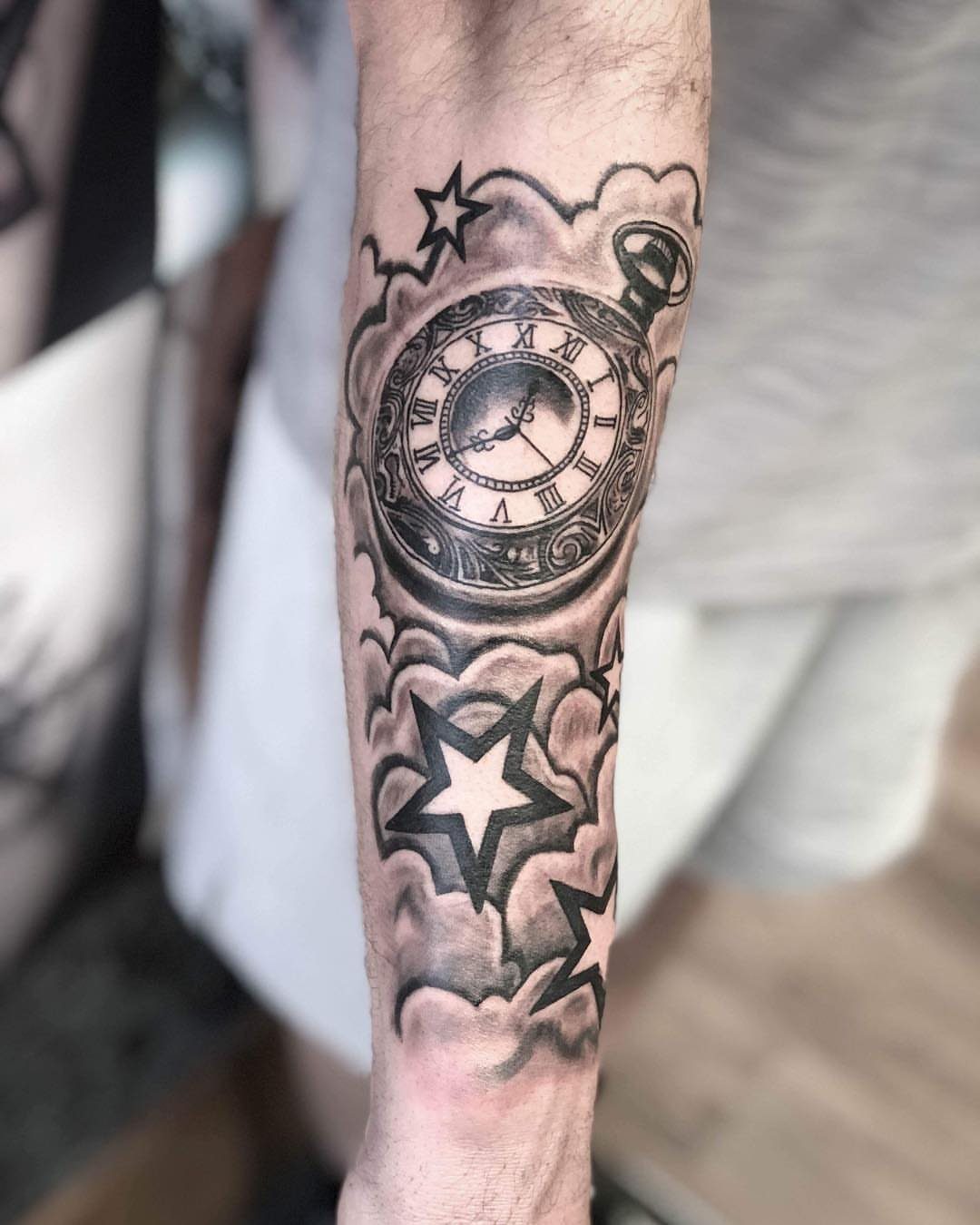 Pocket watch and stars tattoo with clouds on a person's forearm.