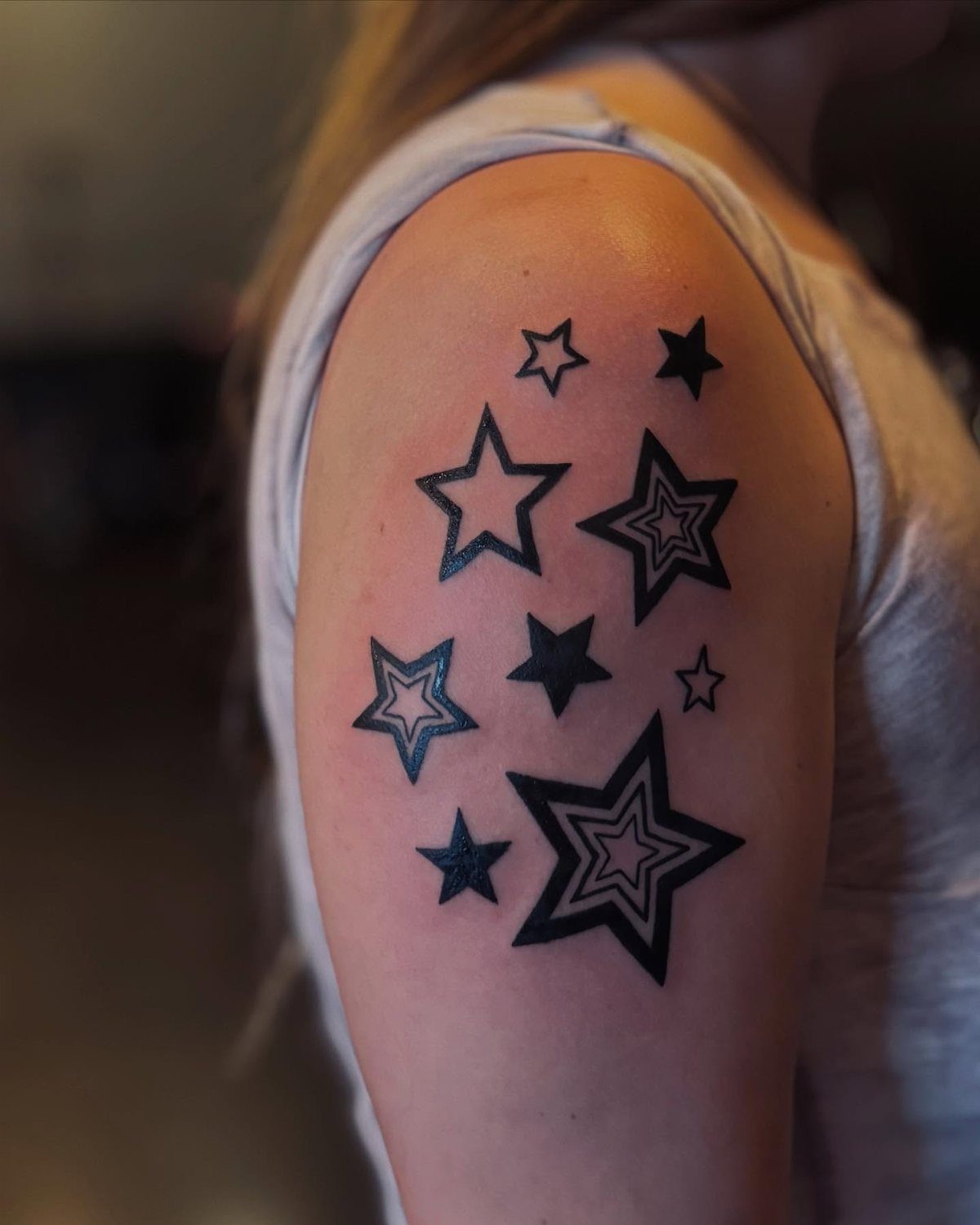 Various black star tattoos of different sizes on a person's upper arm.