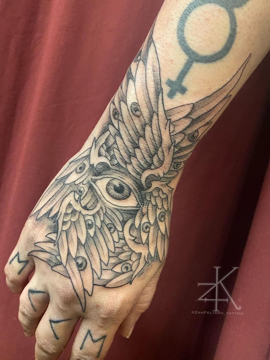Hand tattoo featuring a central eye surrounded by detailed wings and ornate patterns.