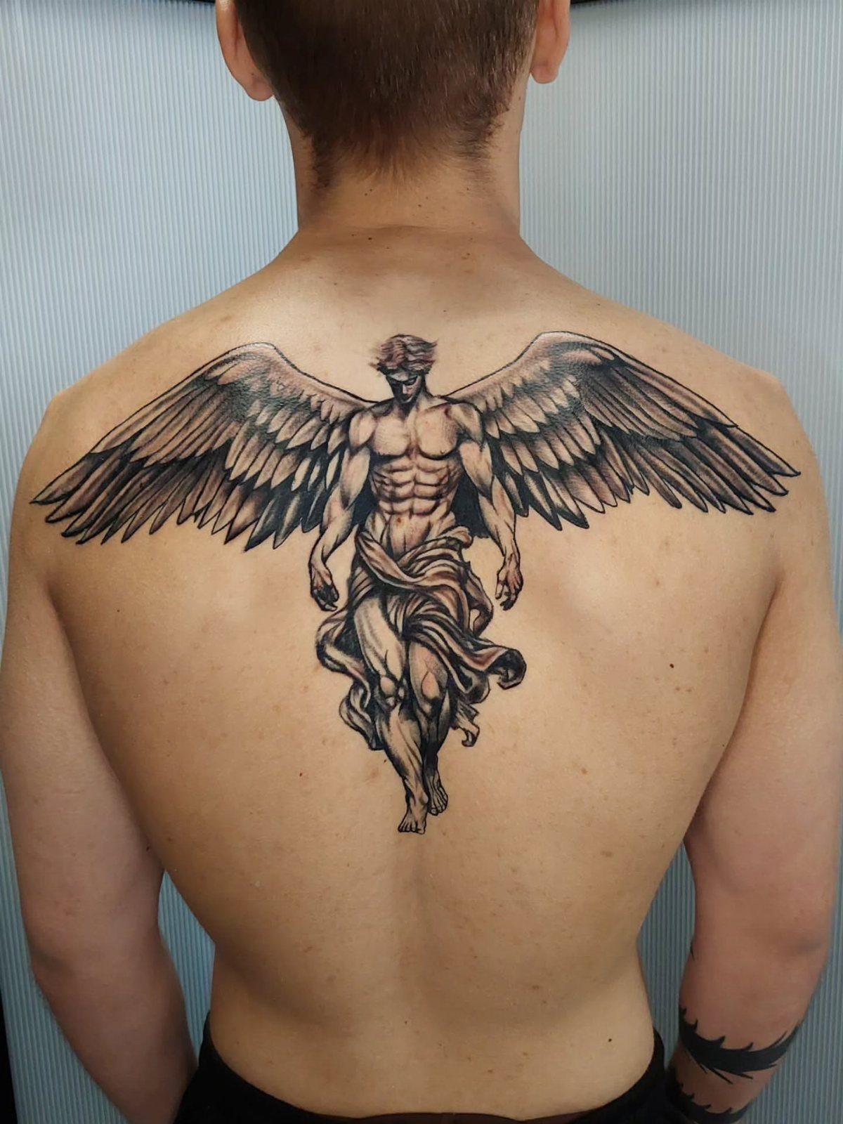 Muscular angel tattoo with large wings spanning across a man's upper back