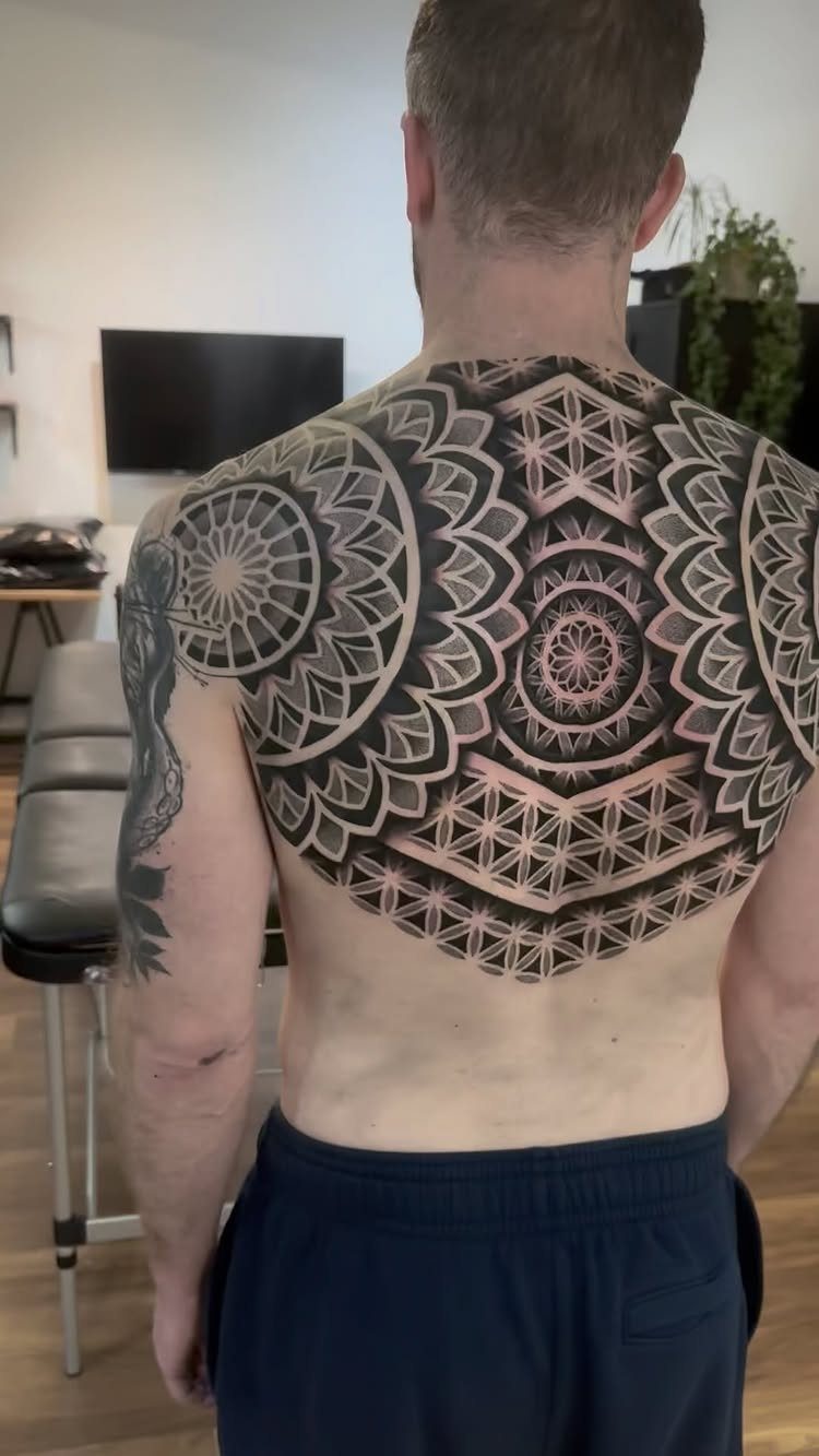 Man's back with a large symmetrical geometric pattern tattoo in black ink