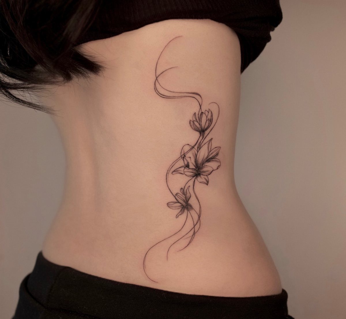Back Ribs Tattoo Ideas: 7 Designs, Vines to Octopus 3 Botanical flower tattoo with flowing lines on a person's side ribcage area.