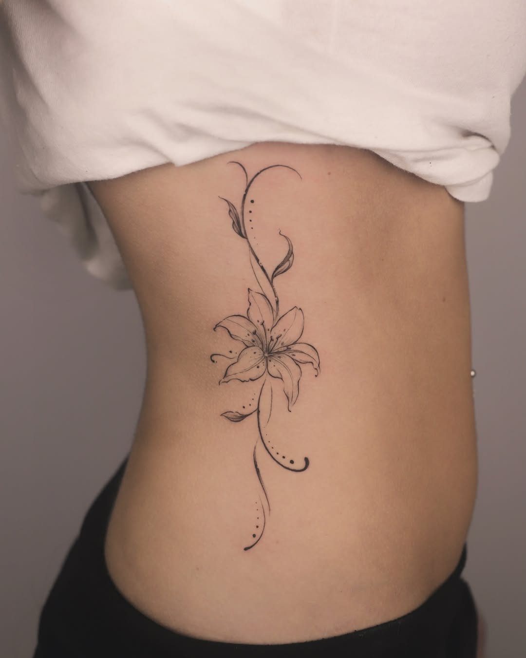 Back Ribs Tattoo Ideas: 7 Designs, Vines to Octopus 1 Lily flower tattoo with swirling vines on a person's side ribcage.