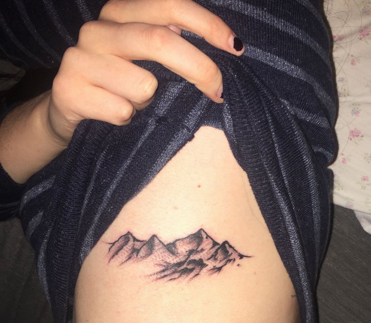Back Ribs Tattoo Ideas: 7 Designs, Vines to Octopus 4 Stippled mountain peaks tattoo on a person's ribs, partially revealed by a striped shirt.