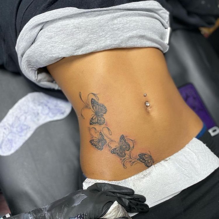 Butterfly tattoos on a stomach next to a silver belly button piercing