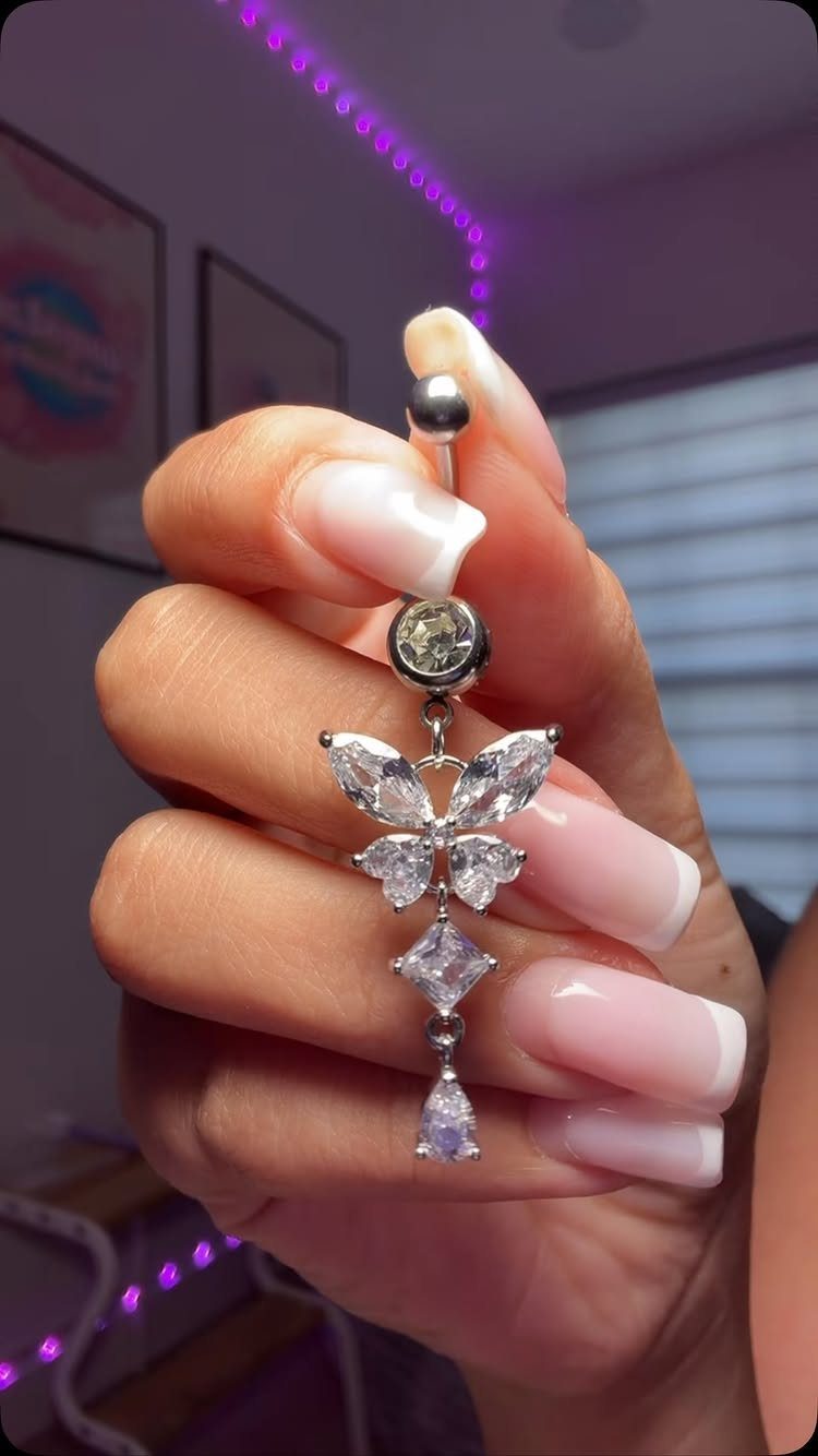 Silver-tone butterfly belly button ring with dangling crystals held by a hand.
