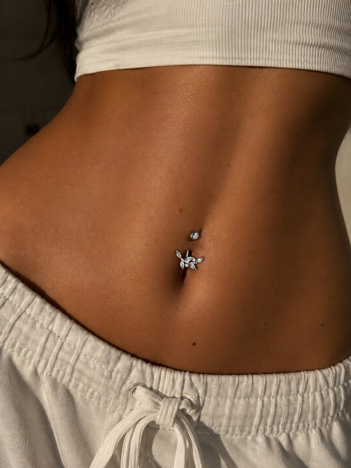 Butterfly-shaped silver belly button piercing with crystals on a person's midriff