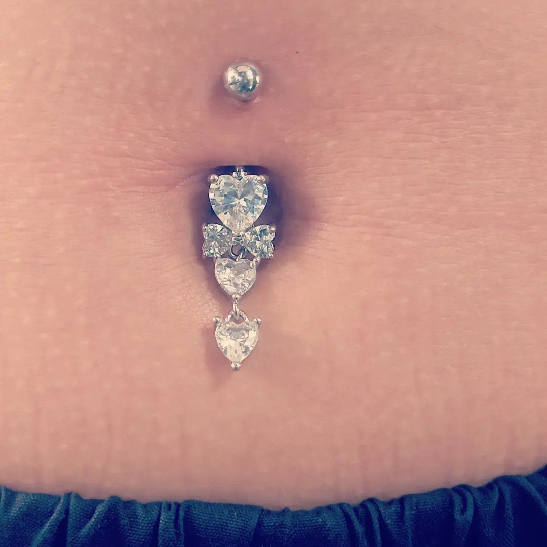Silver-tone belly piercing with clear crystal heart charms dangling from the navel.