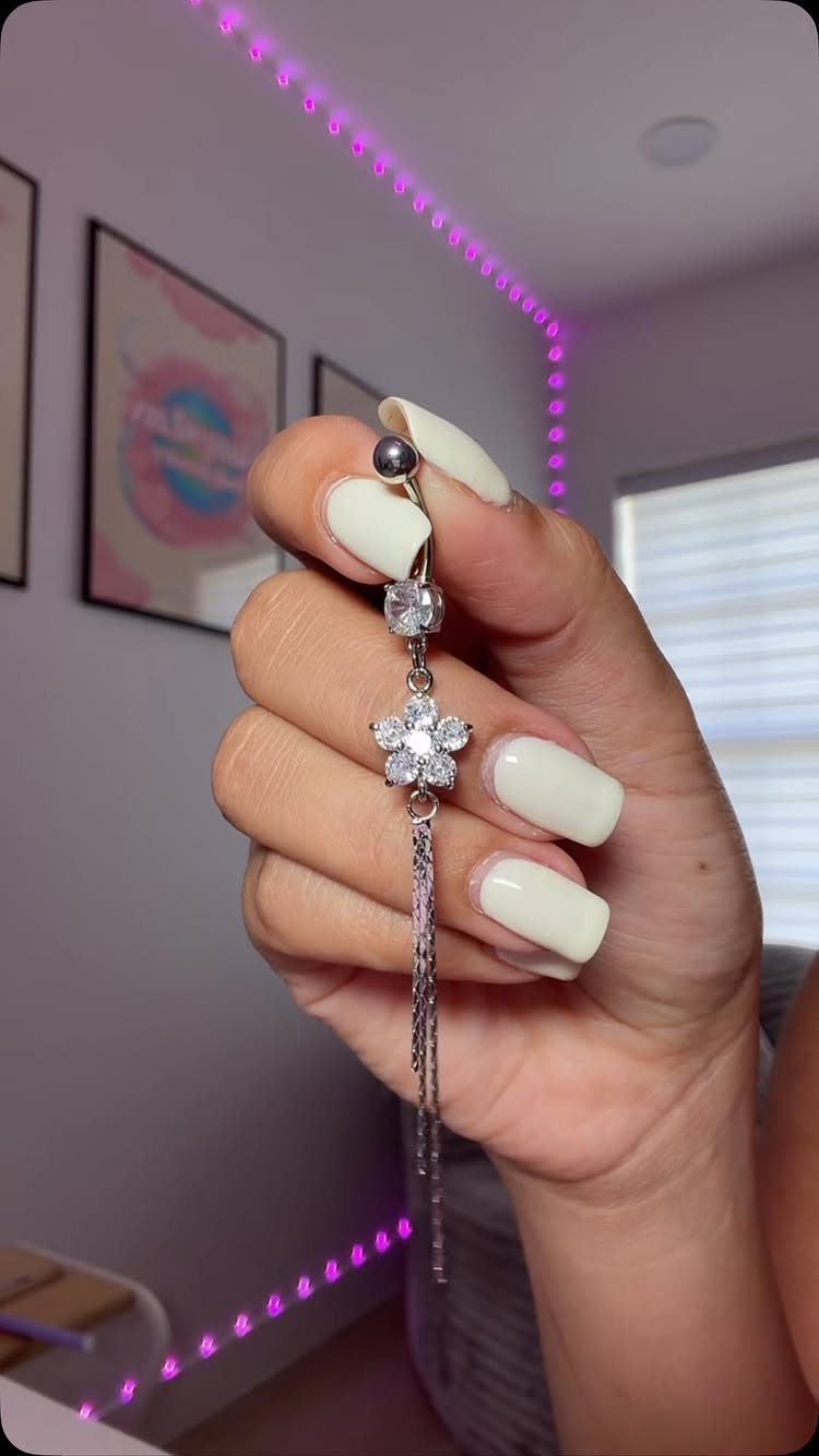 Silver-tone belly piercing barbell with a crystal flower charm and dangling silver chains.