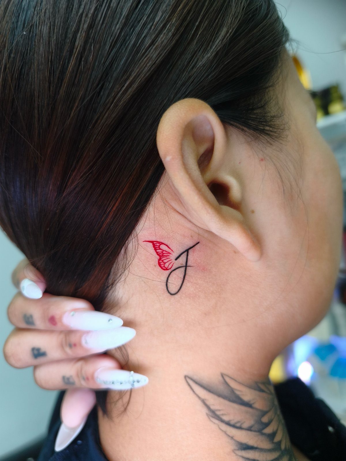 Tattoo of a letter F with a red wing behind a person's ear.