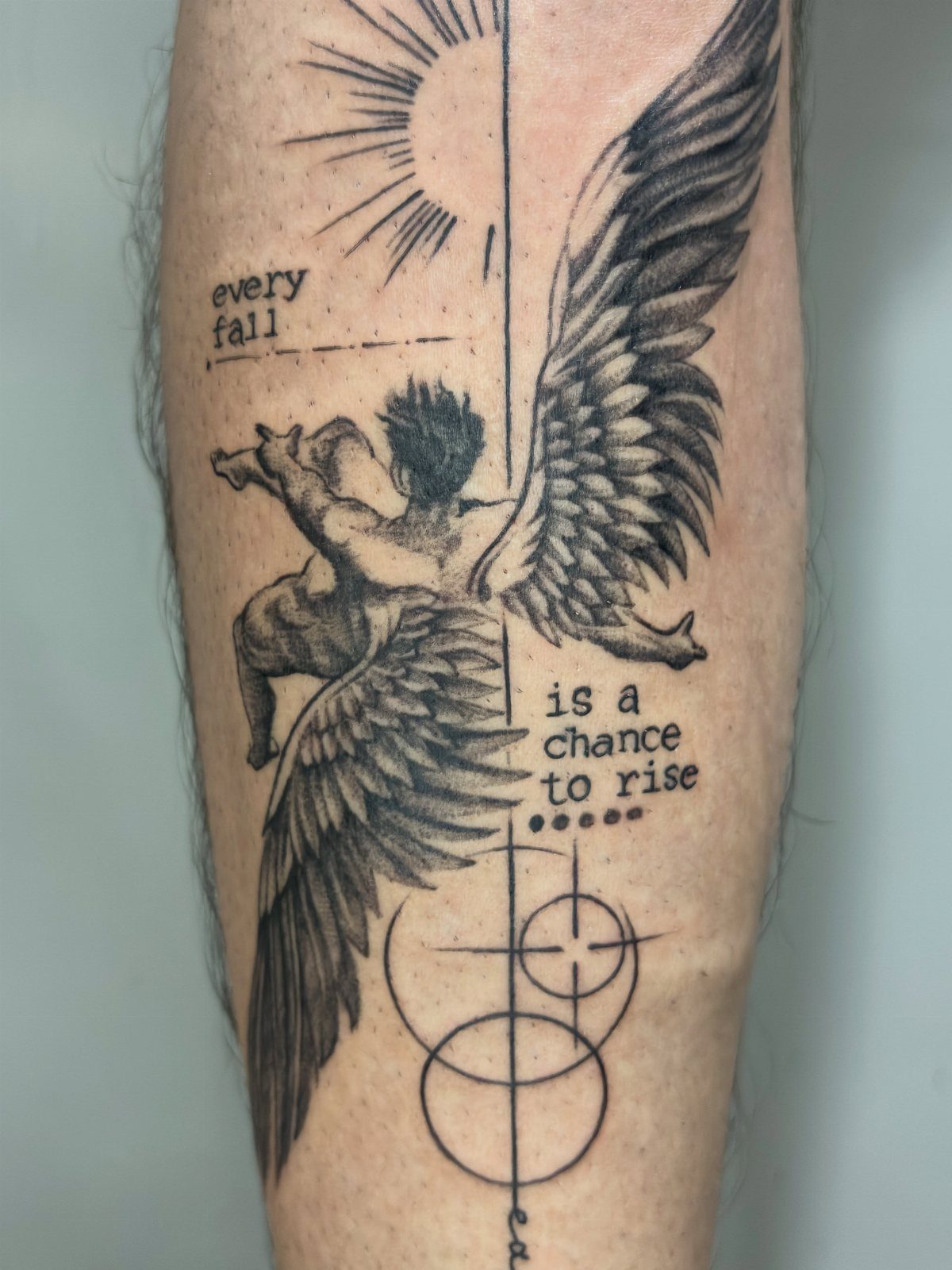 Black and grey tattoo of a winged figure and text on a calf