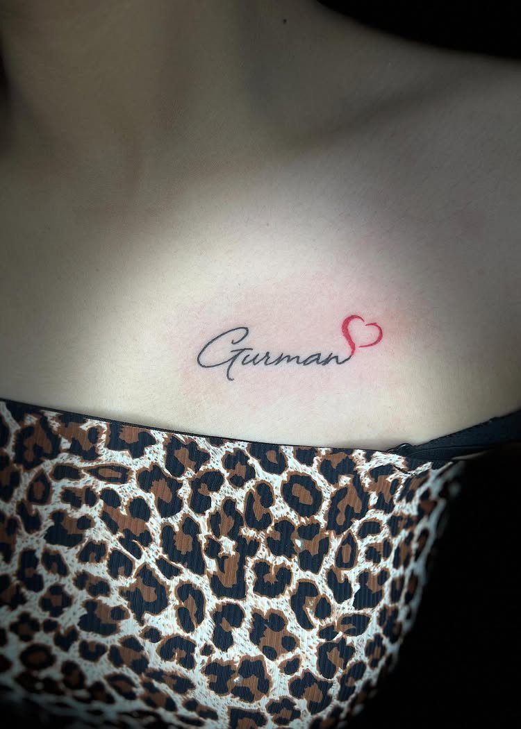 Cursive name tattoo with a red heart on a person's collarbone area