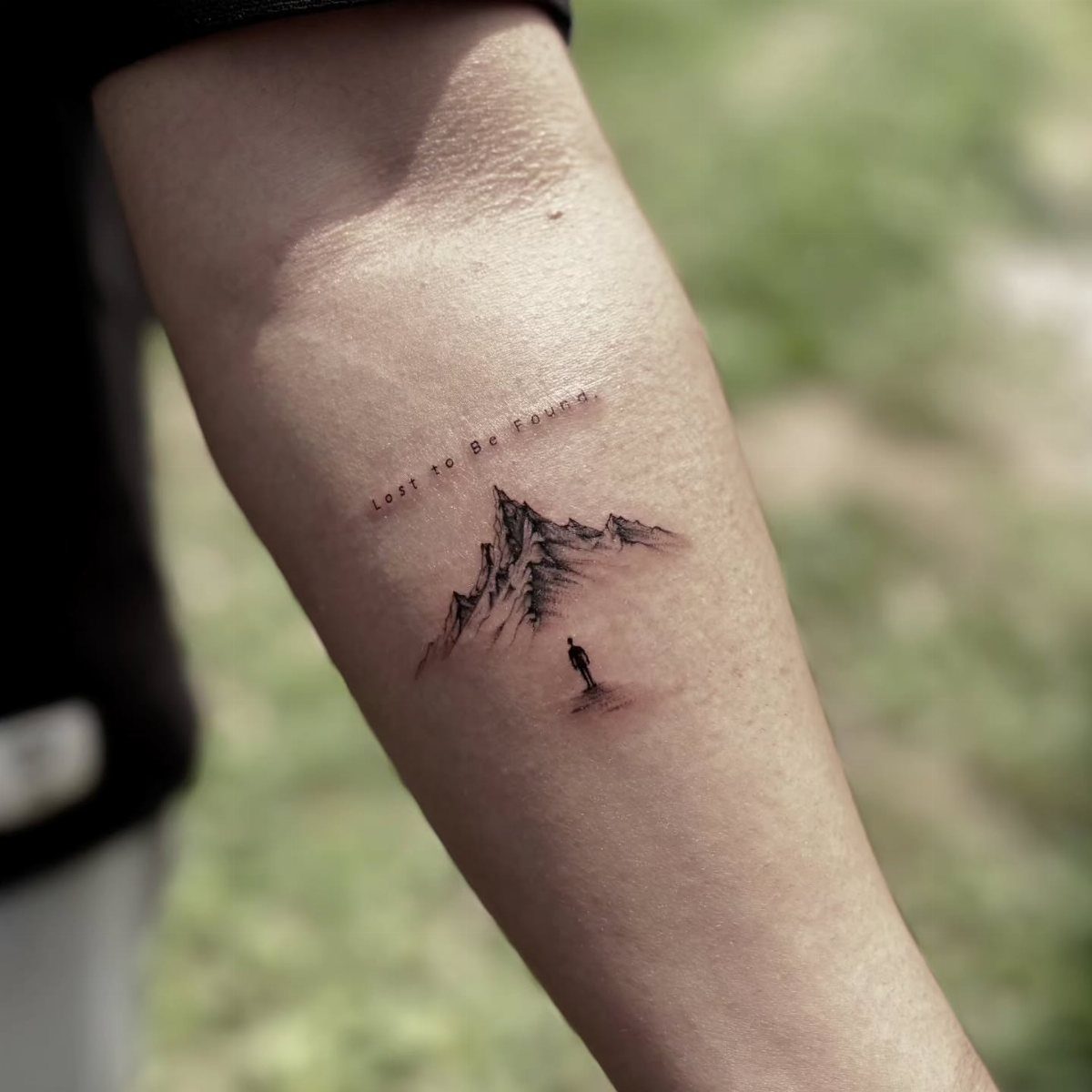 Inner forearm tattoo of a mountain peak with a small silhouette and text.