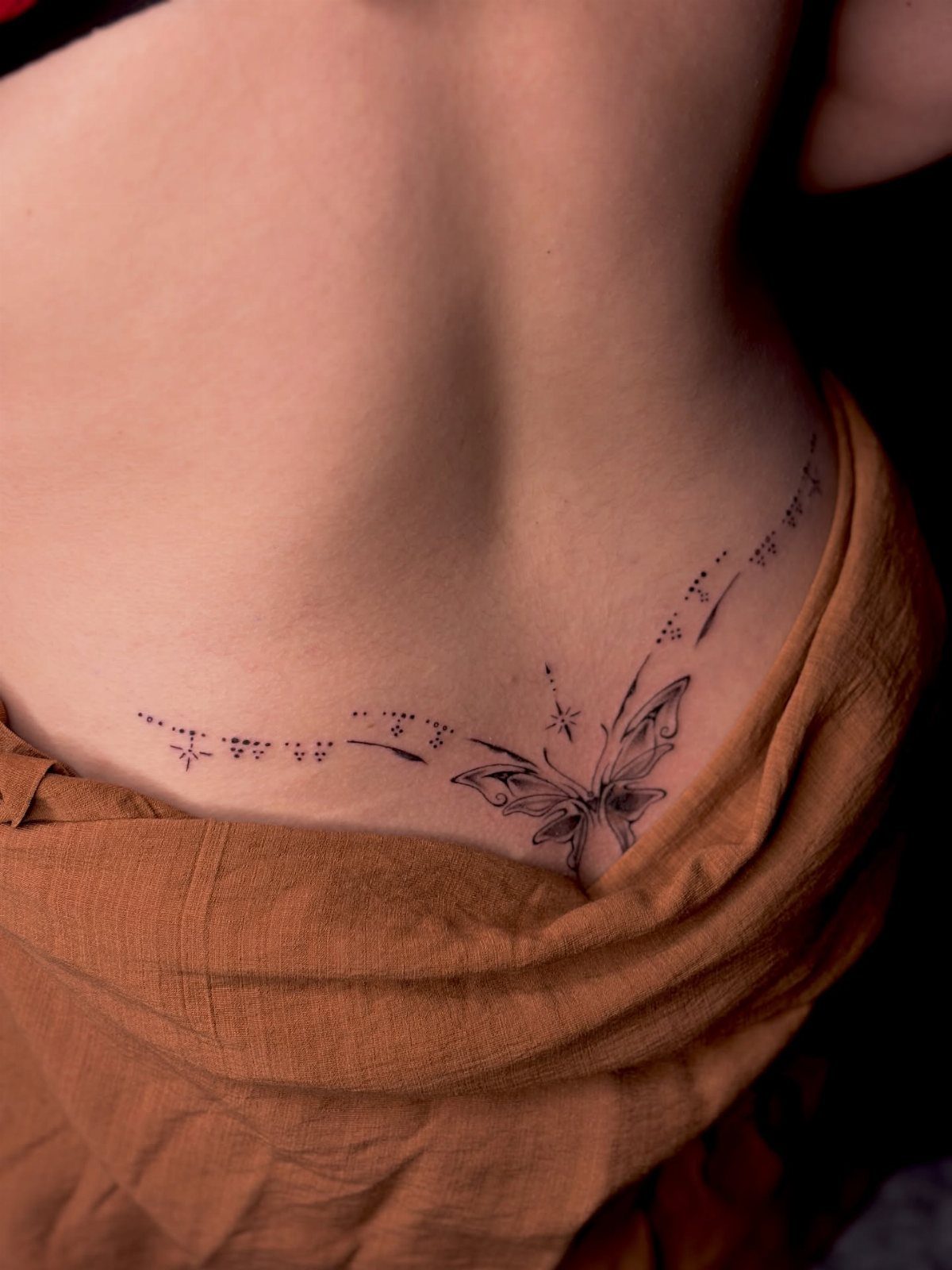 Butterfly tattoo on the lower back of a person wearing brown fabric.