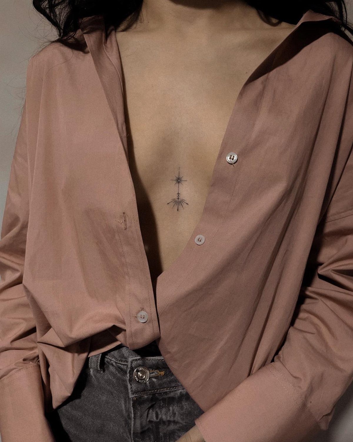 Small black star tattoo on the sternum of a person in a mauve shirt.