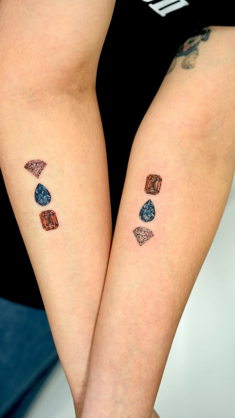 Gemstone tattoos in red, blue, and orange on two person's forearms.