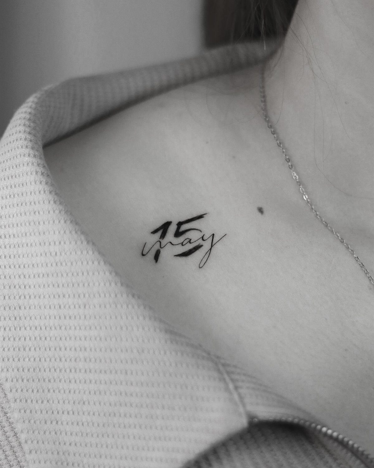 Stylized tattoo of the number 15 and May on a person's collarbone.