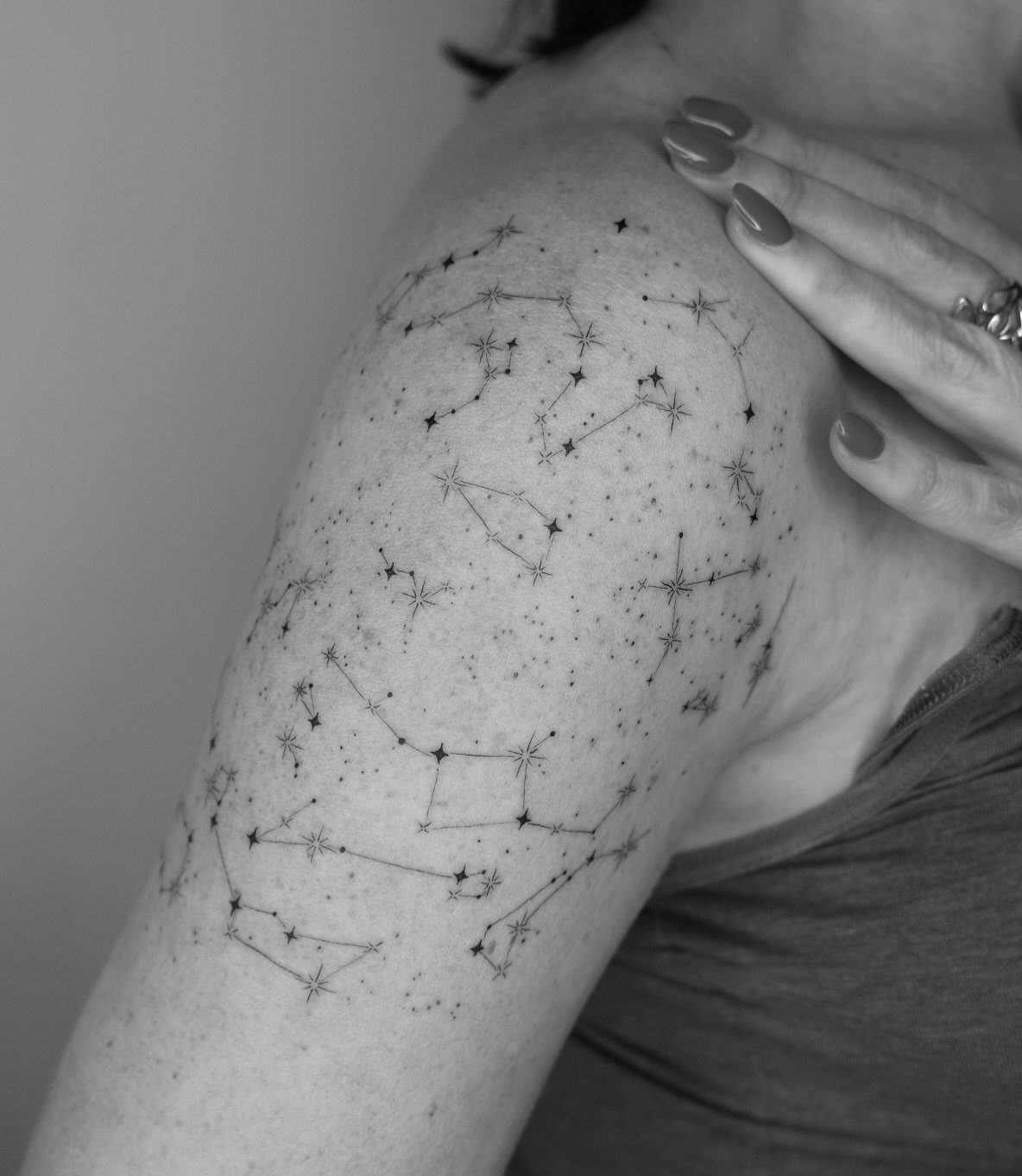Woman's upper arm with several small star constellation tattoos in black ink.