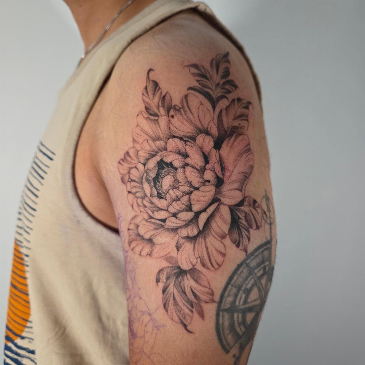 Detailed black and grey shaded peony flower tattoo on a person's upper arm.