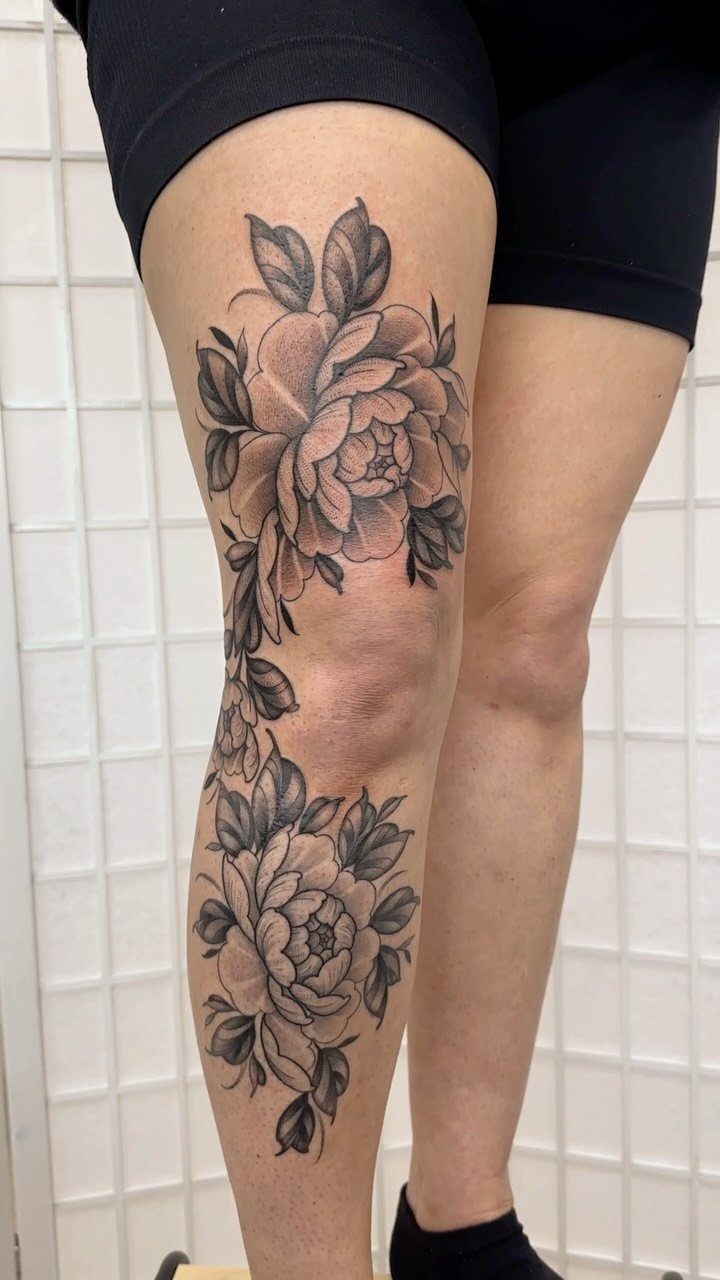 Large black and grey rose tattoos on a person's thigh and lower leg.