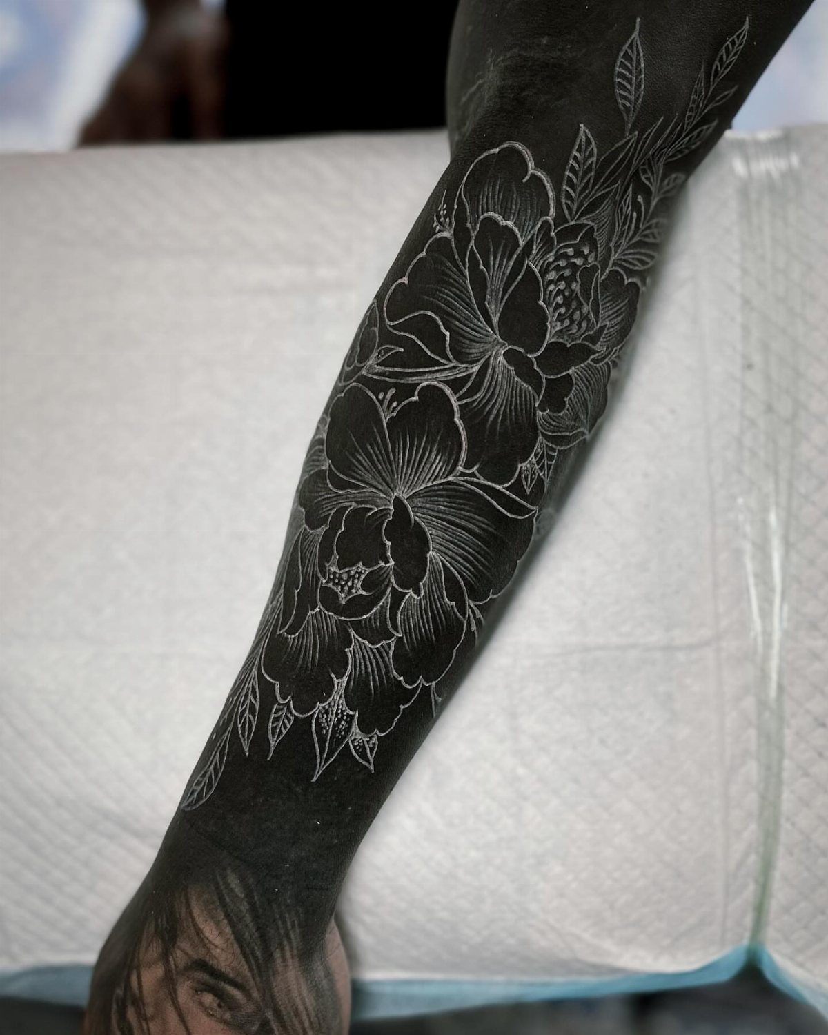 Arm with a blackout tattoo featuring white ink floral peony outlines over solid black.