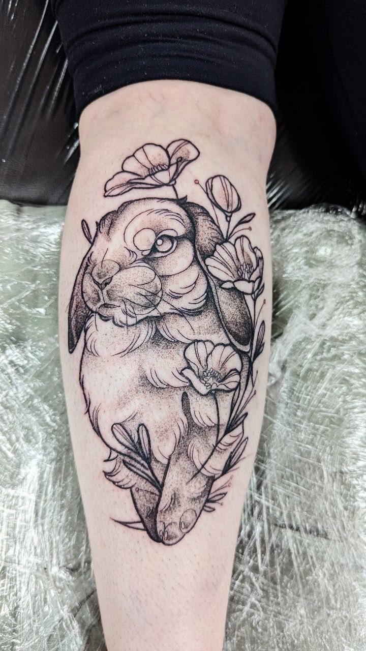 Rabbit and flower tattoo in illustrative blackwork style on a person's leg