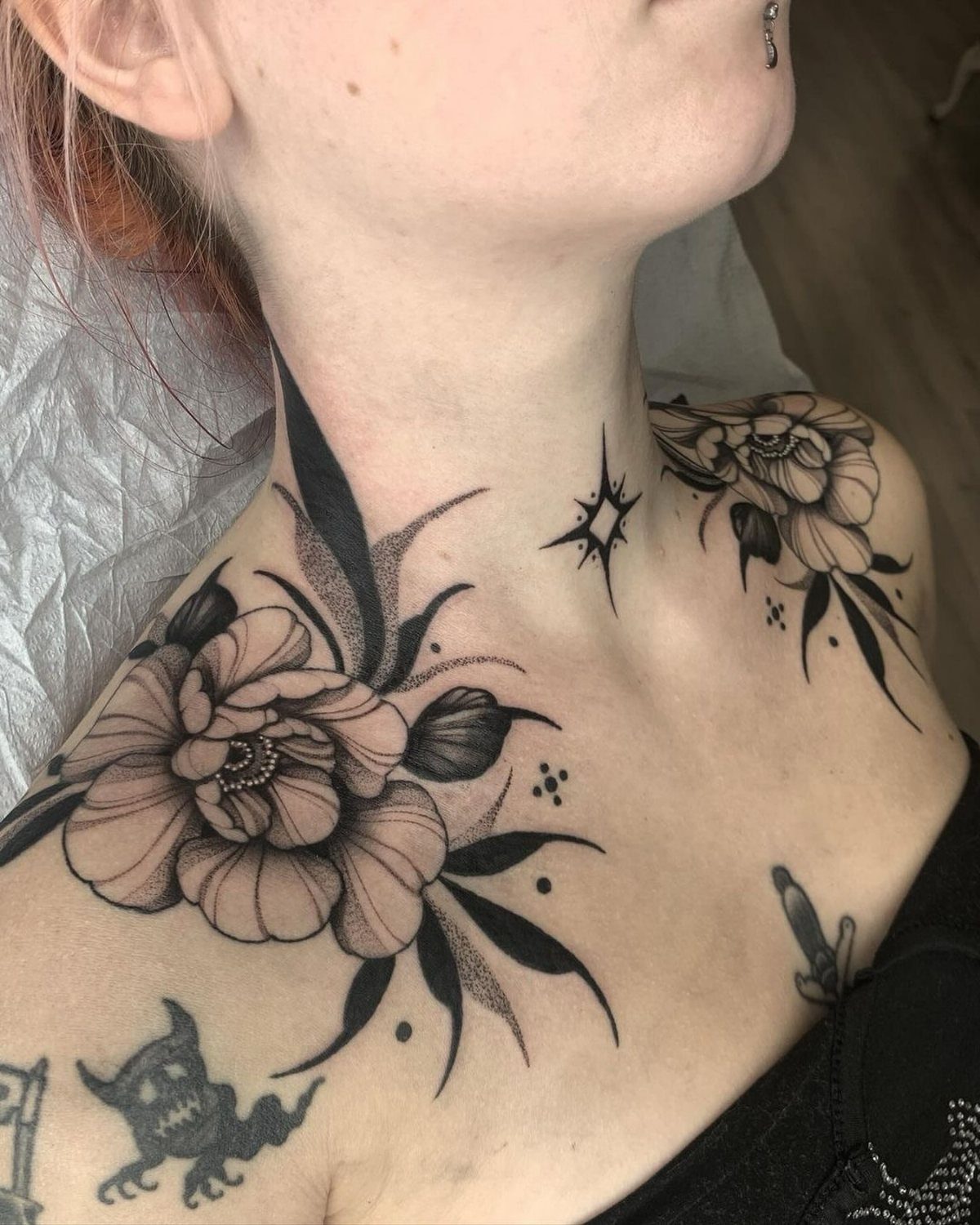 Floral blackwork tattoos of peonies and leaves on a person's neck and collarbone.