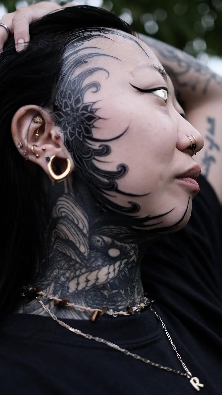 Person with bold blackwork tattoos covering their neck and side of the face.