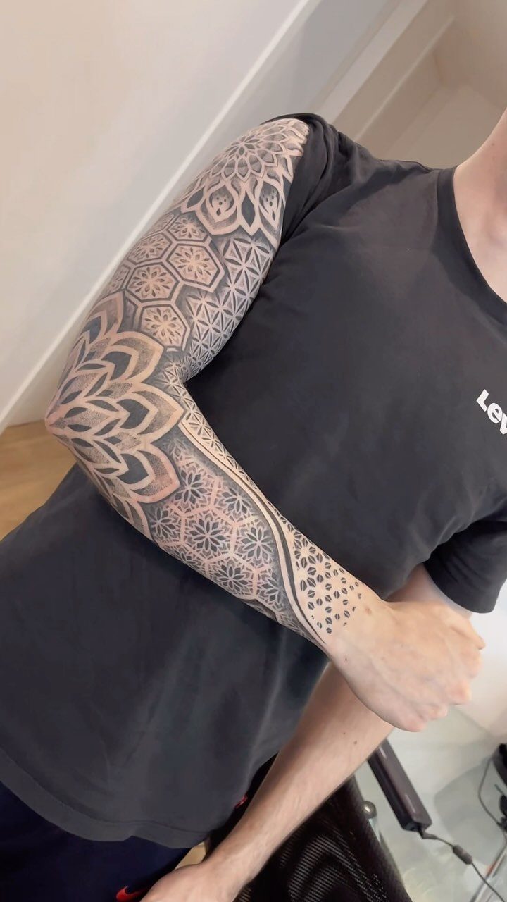 Geometric blackwork sleeve tattoo with mandala patterns and dotwork on a person's arm.