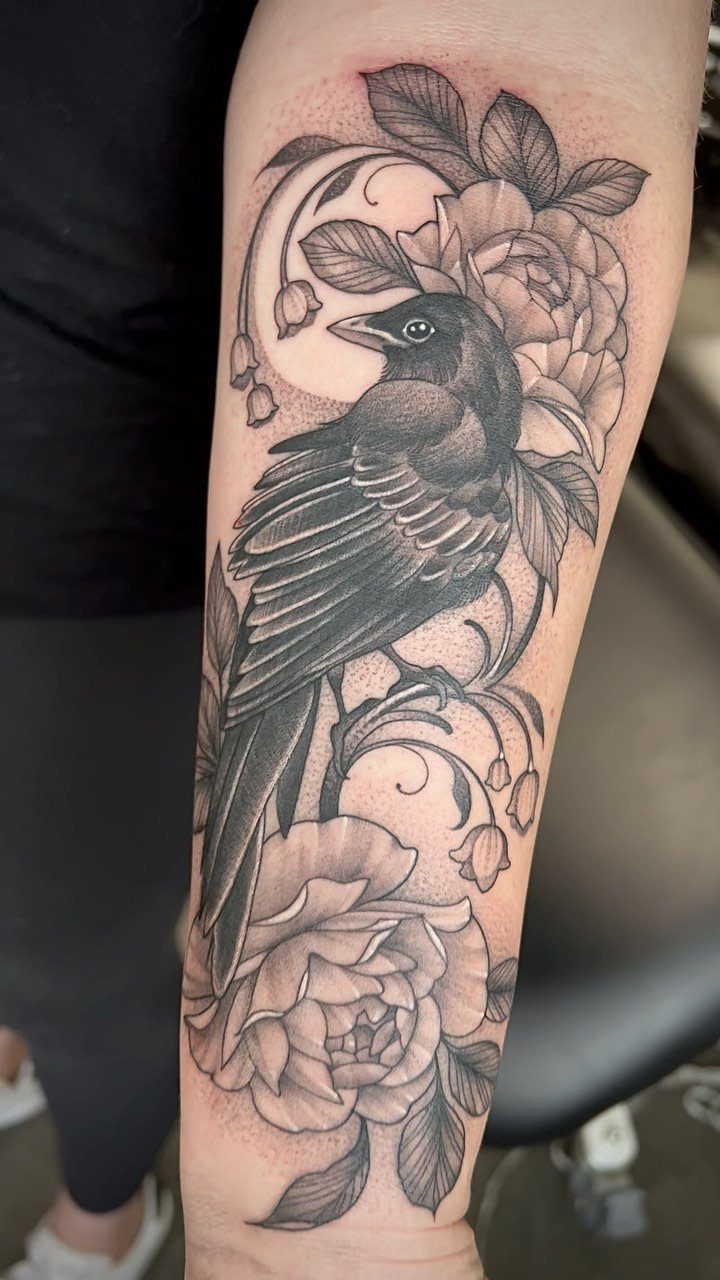 Blackbird tattoo with roses and a crescent moon on a person's forearm