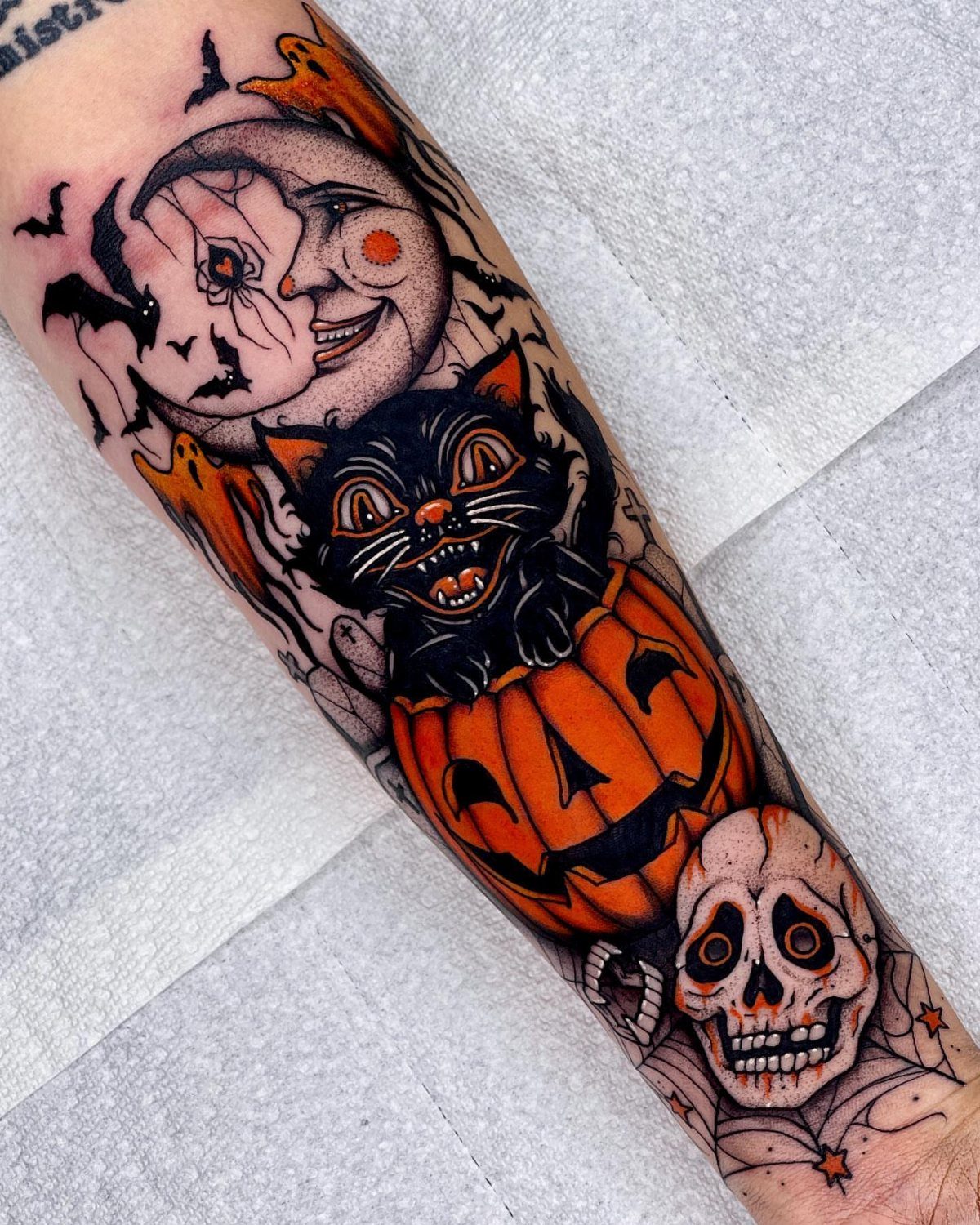 Black cat tattoo emerging from a pumpkin with a skull and crescent moon.