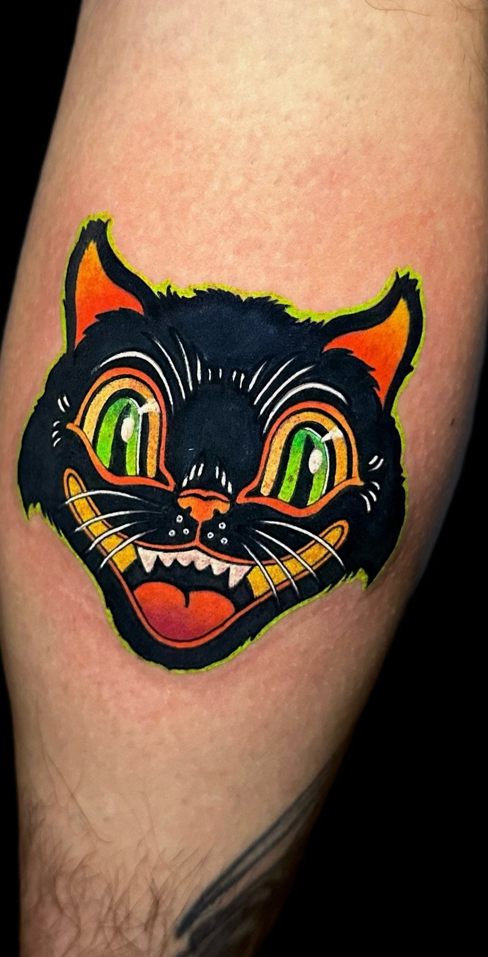 Stylized black cat tattoo with green eyes and orange accents on skin