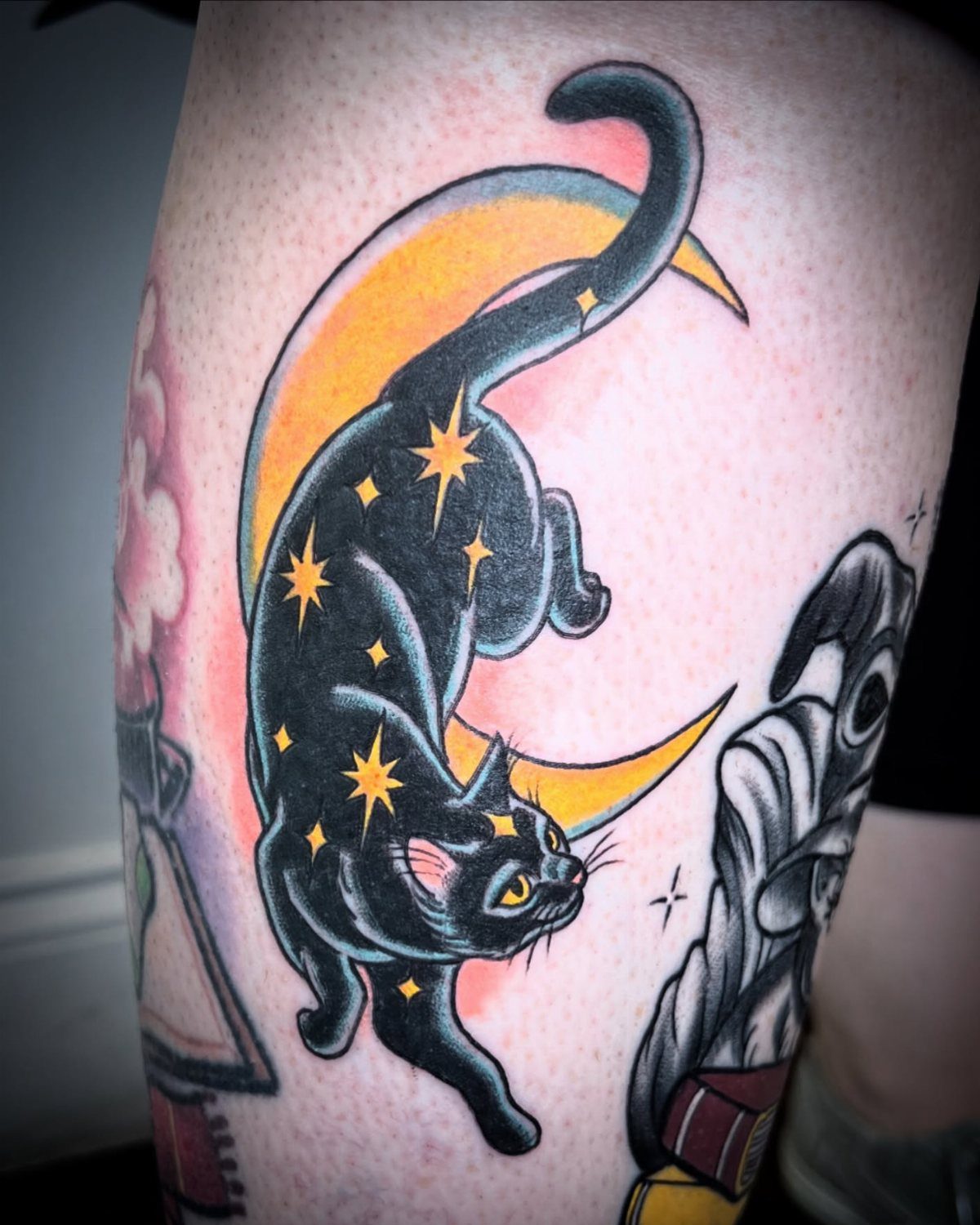 Black cat tattoo with yellow stars leaping across a yellow crescent moon.