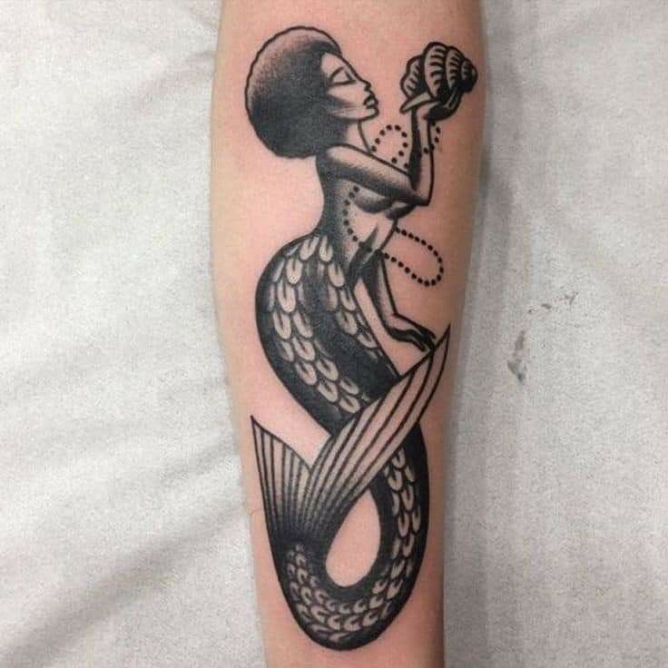 8 Black Mermaid Tattoo Ideas with Afro, Locs and Scales 5 Black mermaid tattoo with an afro holding a seashell to her ear.