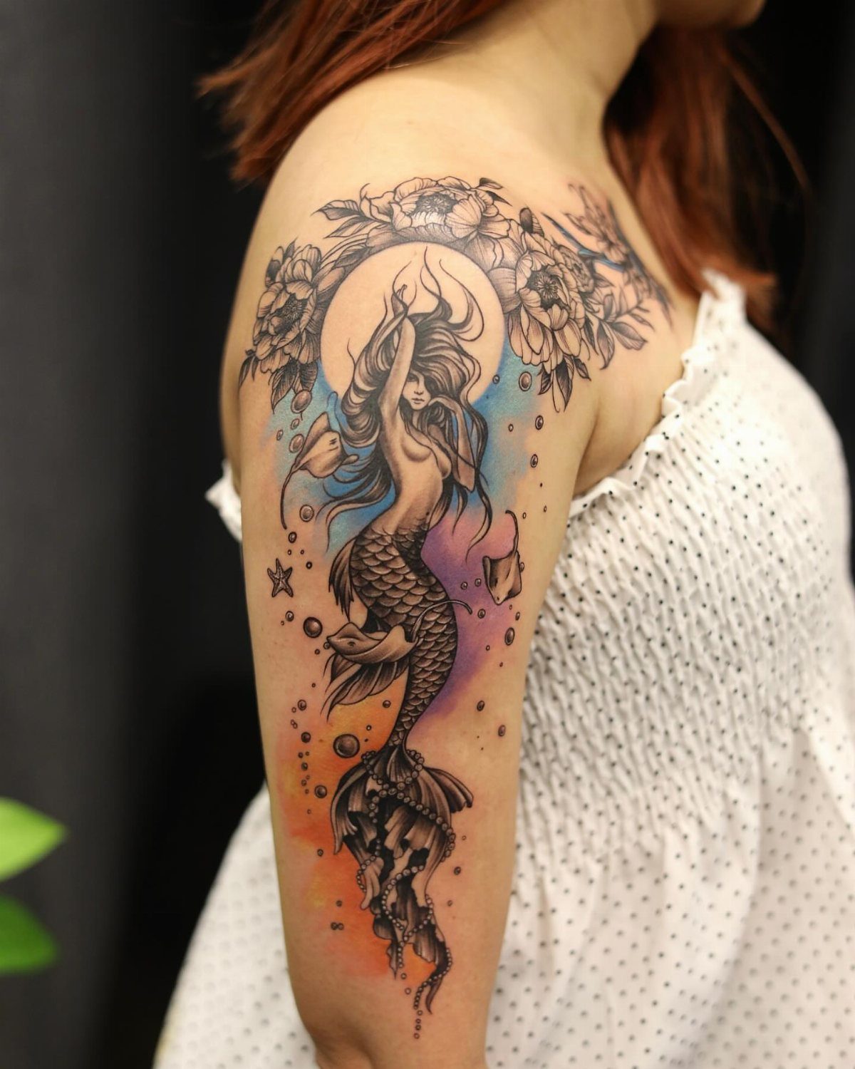 8 Black Mermaid Tattoo Ideas with Afro, Locs and Scales 4 Mermaid tattoo on an arm with flowing hair, flowers, and colorful background.