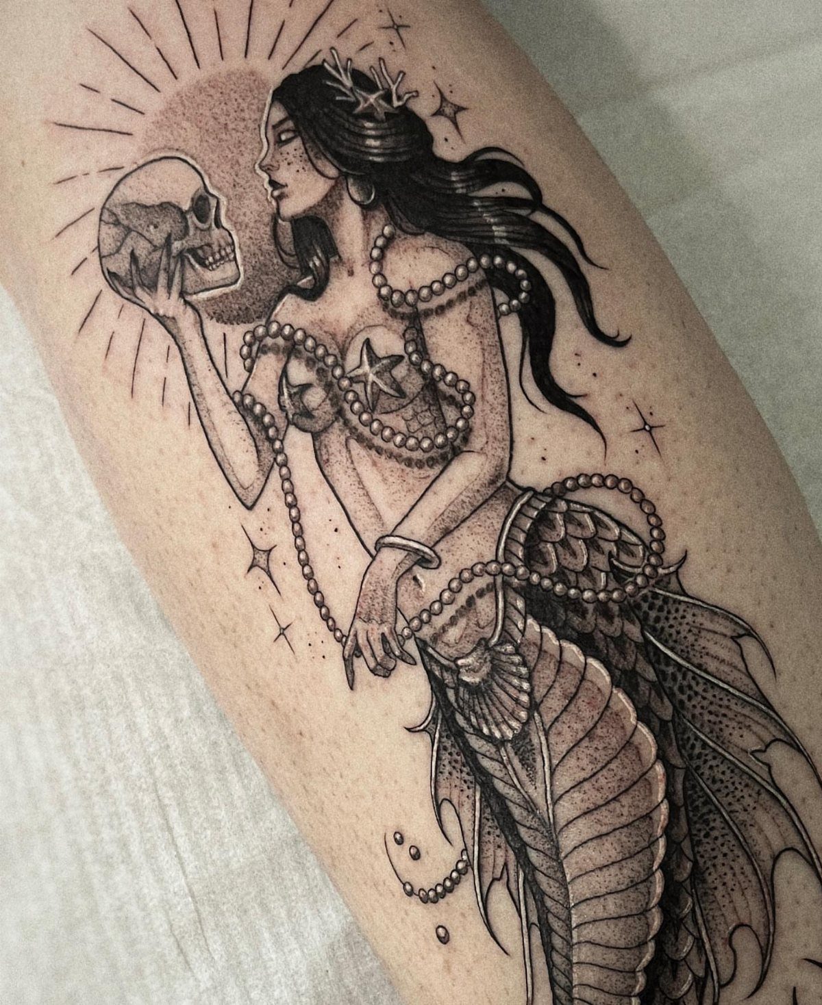 8 Black Mermaid Tattoo Ideas with Afro, Locs and Scales 7 Mermaid tattoo with ornate scales on a tail, holding a skull on skin.
