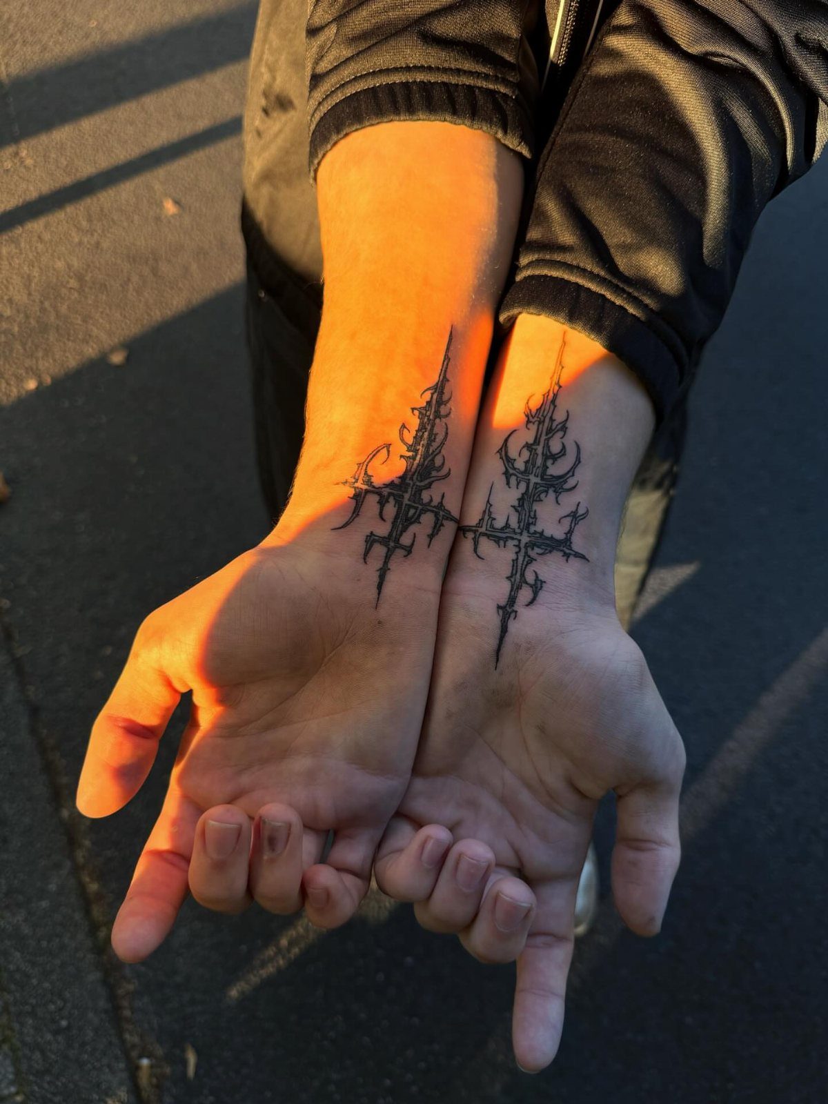 Stylized black ink cross tattoo spanning across two open palms and wrists.
