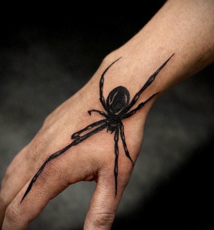 Spider tattoo with long legs inked in black on the back of a hand.