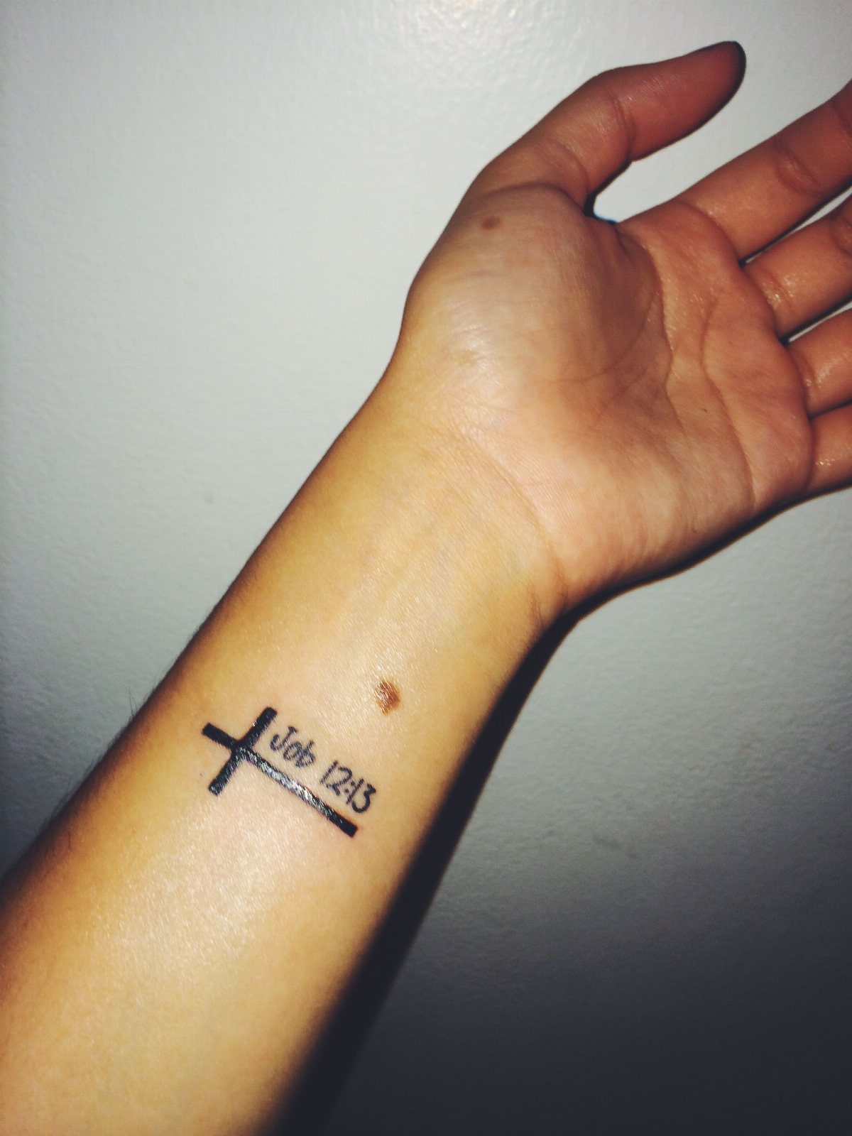 Wrist tattoo of a small cross and the biblical reference Job 12:13.