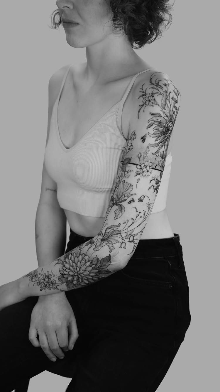 Botanical tattoo sleeve with fine-line black ink flowers and leaves on an arm.