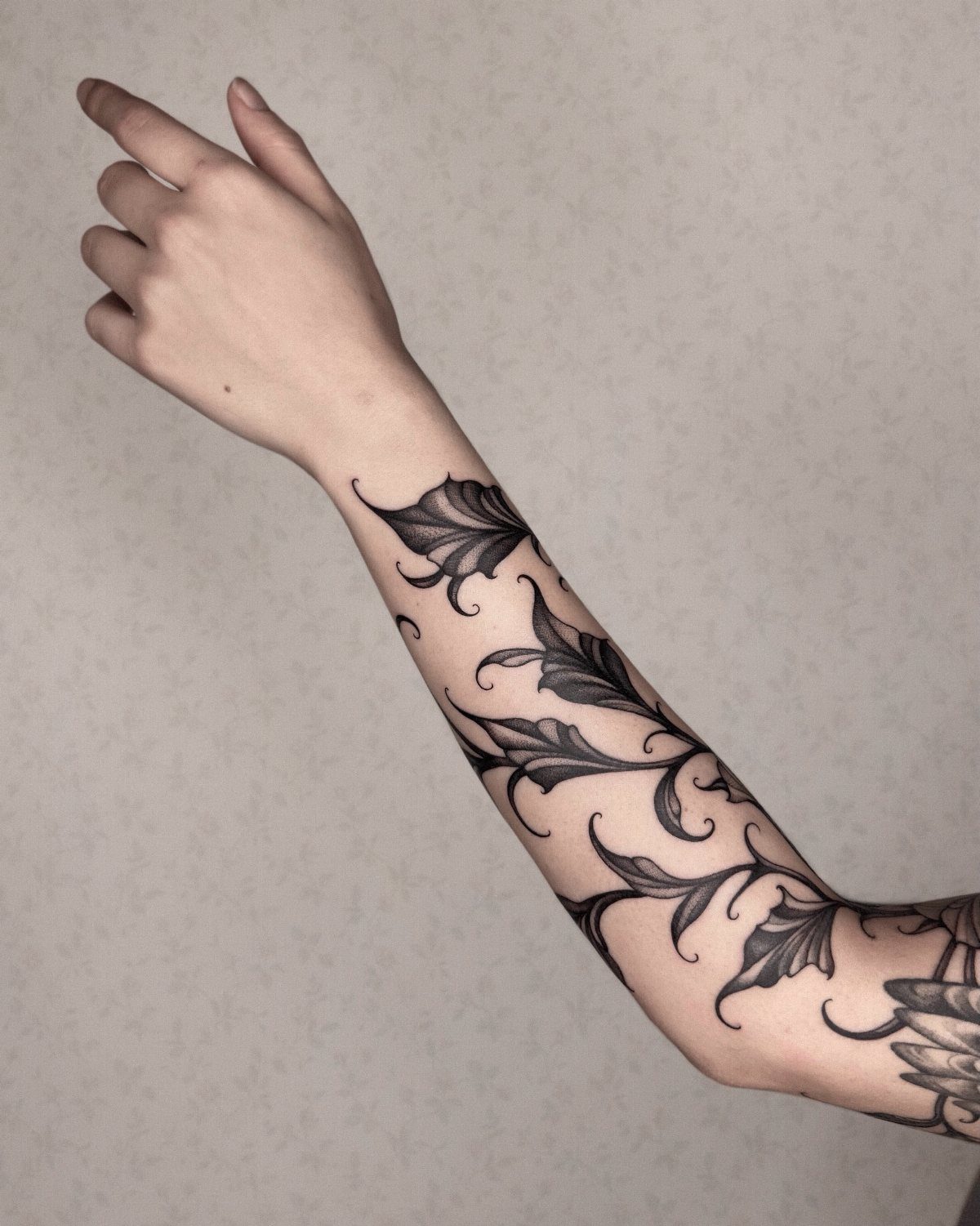 Black ink tattoo of climbing ivy vines and leaves on a person's forearm