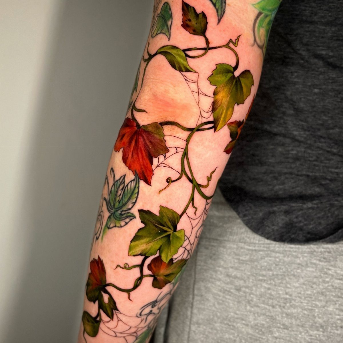 Ivy vine tattoo with green and red leaves wrapping around a person's arm.