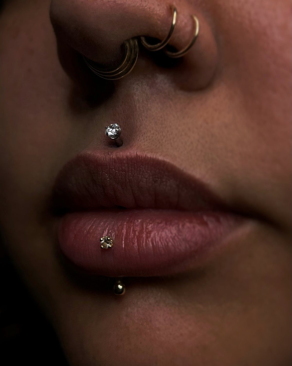 Center Lip Piercing Ideas: 7 Styles to Consider 6 Person with gold nose rings and gemstone piercings in the philtrum and lower lip.