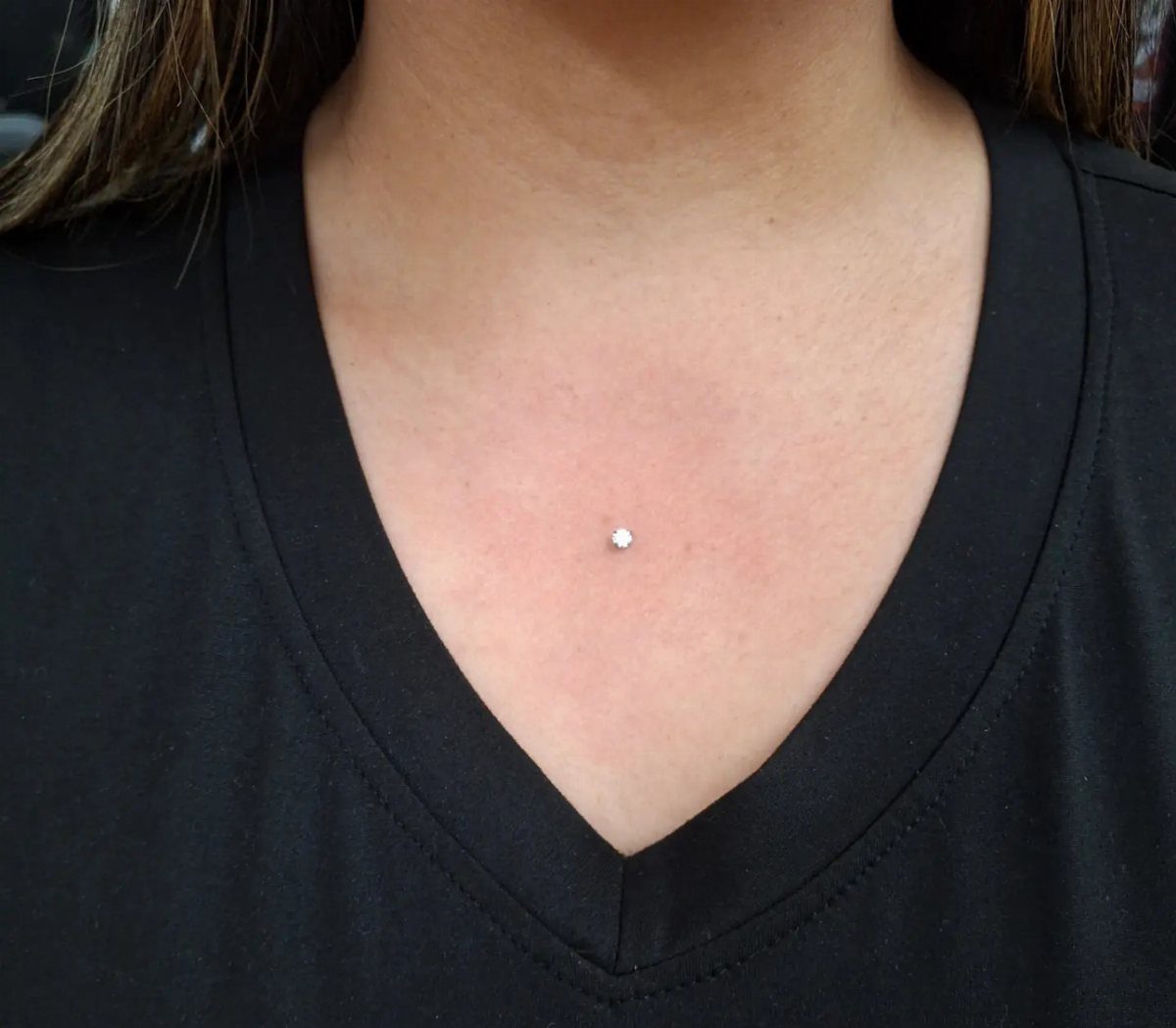 Small silver gemstone dermal piercing centered on a person's upper chest skin.