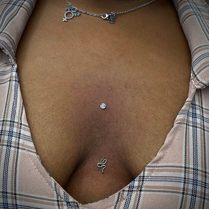 Chest piercings featuring a small gemstone stud and a silver snake-shaped jewelry piece.