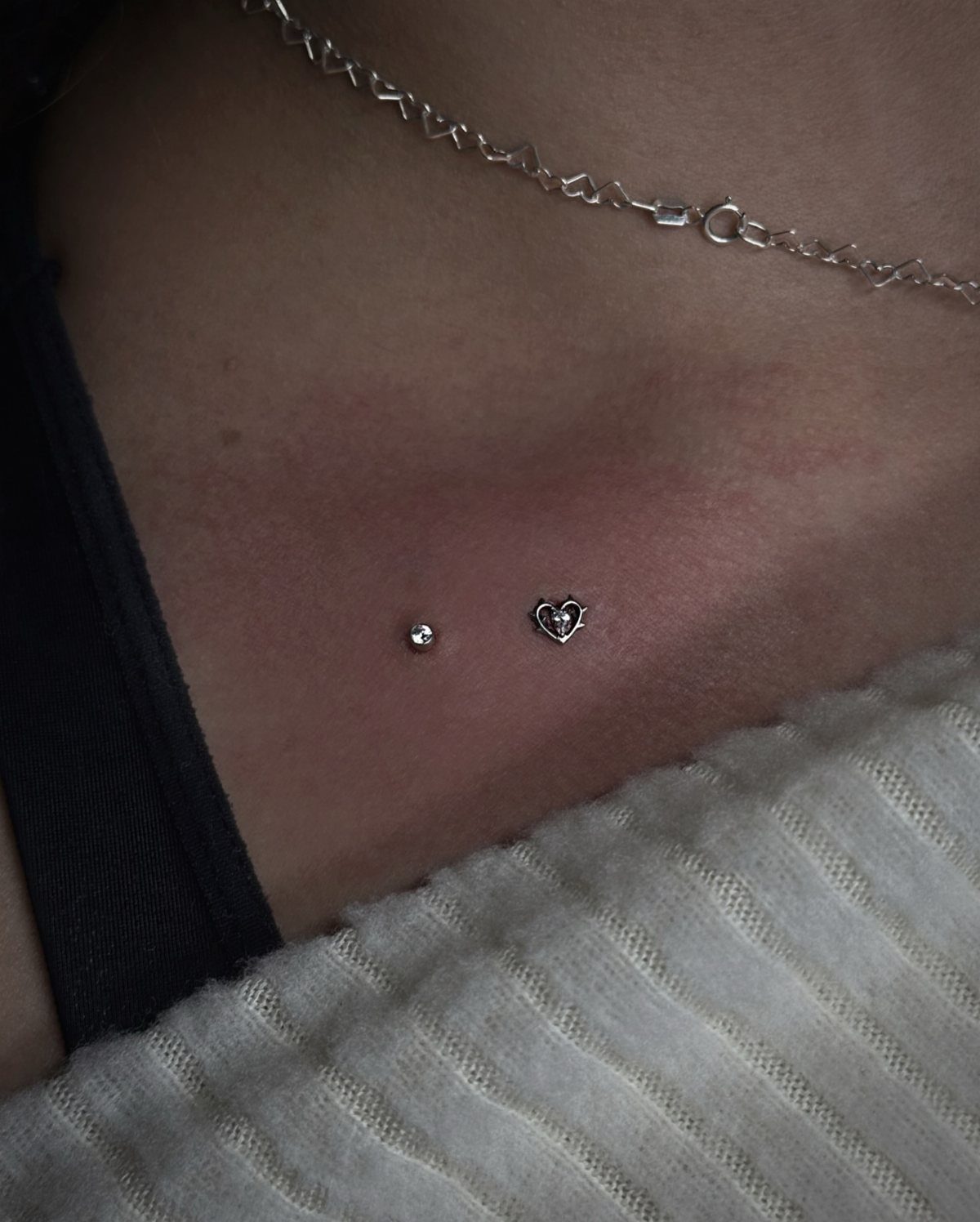 Chest piercings featuring a small silver stud and a heart-shaped jewel on skin.