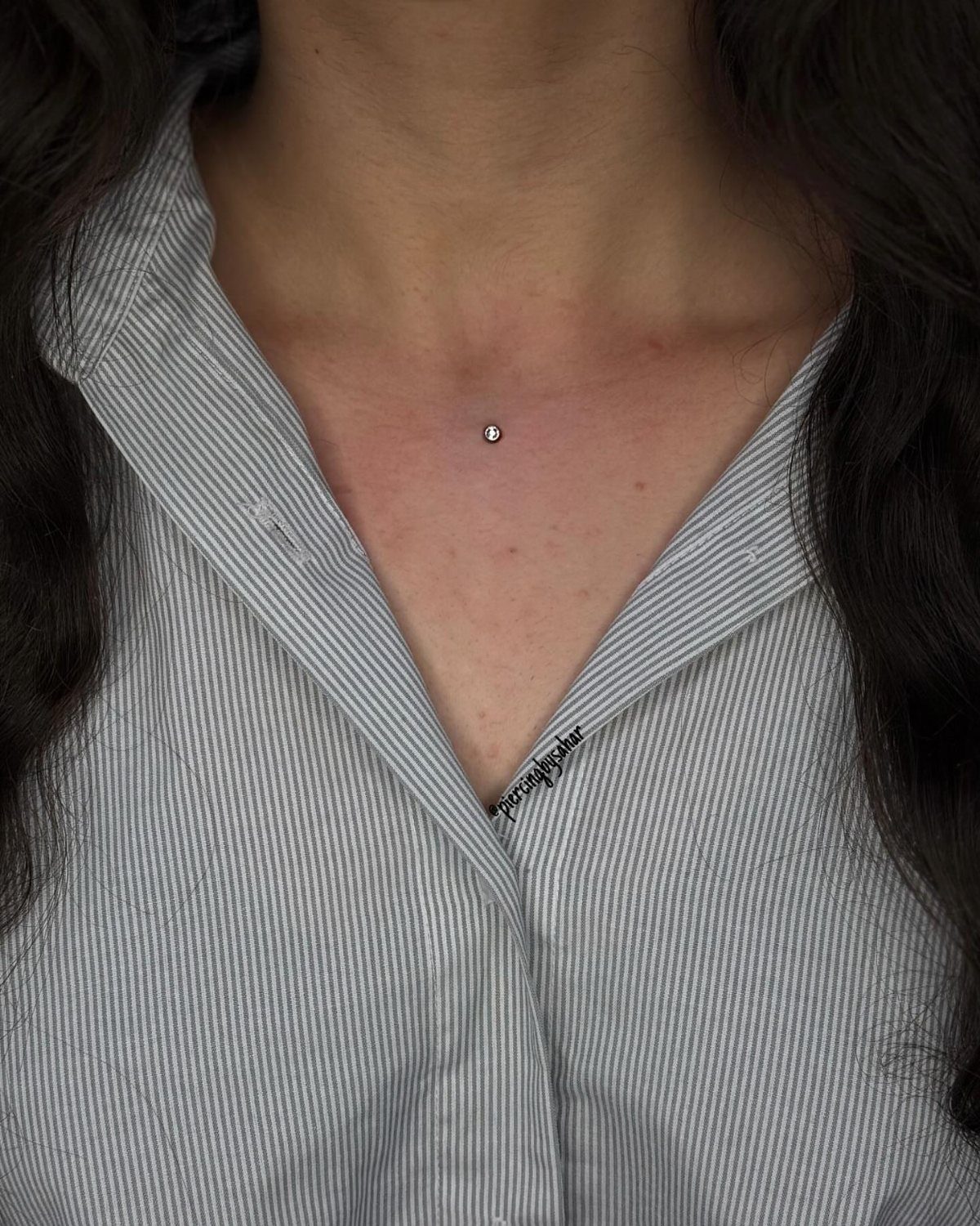 Chest area of a person wearing a striped shirt with a silver stud piercing.